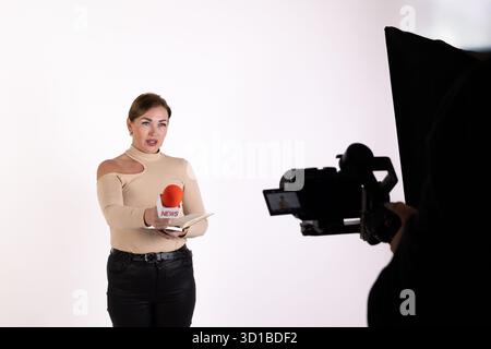 A reporter is being filmed while holding a microphone during a news broadcast Stock Photo