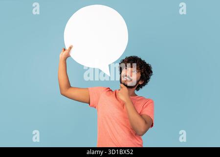 Pensive Indian Man Holding Blank Speech Bubble Considers His Thoughts in a Blue Studio Stock Photo
