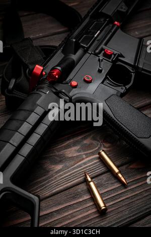 Close-up of a black tactical rifle with red accents and two bullets on dark wood. Stock Photo