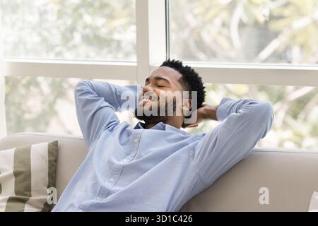 Young African man reclining on cozy sofa with peaceful expression Stock Photo