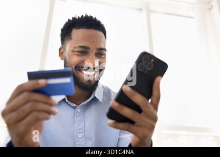Smiling African guy holding card and smartphone, closeup Stock Photo