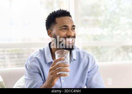 Handsome man sit on sofa with glass of still water Stock Photo