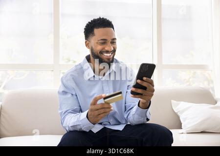 Man sit on sofa with credit card and mobile phone Stock Photo