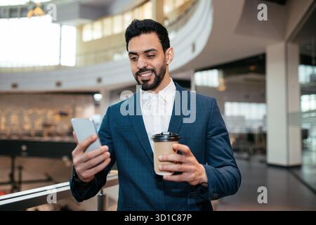Professional Man Enjoying Coffee While Using Smartphone in Modern Office Setting Stock Photo