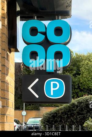 Vertical sign for Co-op supermarket with parking direction mounted on a brick wall in front of greenery and clear skies Prudhoe northumberland Stock Photo