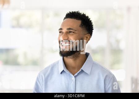 Headshot portrait optimistic African man looks into distance and laughing Stock Photo