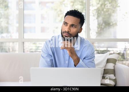 Pensive guy working on laptop looking away with thoughtful expression Stock Photo