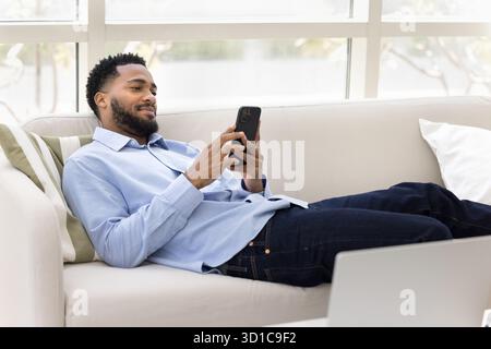 Relaxed African man spend free time on internet using smartphone Stock Photo