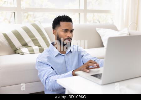 Serious African man sitting on floor, working on laptop Stock Photo