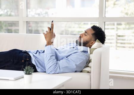 Young man lying on sofa while using his smartphone Stock Photo