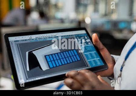 Close up of engineer using CAD app on tablet to optimize sustainable solar cells device fabrication. Clean energy professional innovates solar powered gadget prototype using touchscreen device Stock Photo