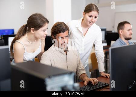 Two female friend companions stands next to computer courses male student Stock Photo