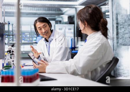 Coworkers talking, doing genetics study using clinical equipment in medical lab. Team of biotechnologists doing brainstorming, using scientific gear in research facility, doing complex experiments Stock Photo