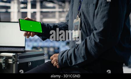 Data center worker uses isolated screen smartphone while deploying deep learning software. Server hub employee uses chroma key mobile phone while training AI systems with datasets, camera B Stock Photo