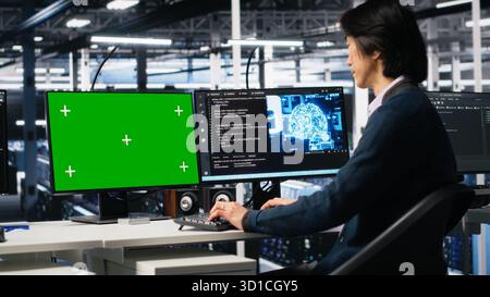 Data center admin typing on isolated screen PC keyboard, using AI. IT specialist at work using artificial intelligence on chroma key computer to oversee servers powering deep learning, camera A Stock Photo