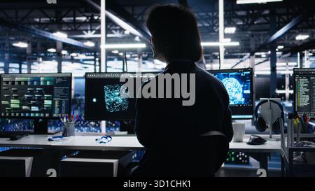 Data center software developer using computer to monitor neural network AI LLM visualization. Worker in high tech facility using PC to oversee servers powering machine learning processes, camera A Stock Photo