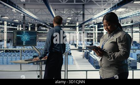 Team of data center technicians checks AI dashboard using laptop during systems review. Teamworking server hub colleagues test artificial intelligence tools on notebook, camera A Stock Photo