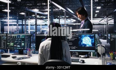 Team leader supervising technicians in server room using AI to review infrastructure diagnostics. Asian man in data center analyzing performance of workers using artificial intelligence, camera A Stock Photo