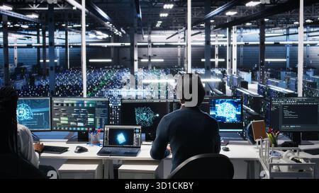 Programmer entering server room office, using AI to review infrastructure diagnostics. IT admin in data center high tech facility analyzes performance data using artificial intelligence tech, camera A Stock Photo