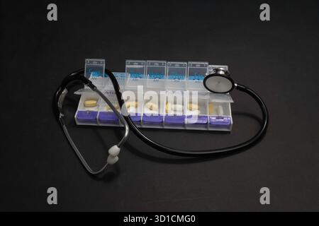 A Stethoscope laying on top of an open, full pill box. Viewed straight on from a high view point, on a black background. Stock Photo