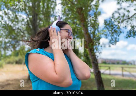 Woman smiling, dancing to music, enjoying freedom and relaxation with unicorn headphones outdoors Stock Photo