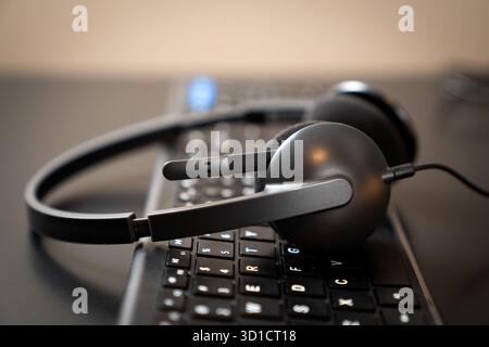 Low angle shot of a black headset with a microphone resting on a black computer keyboard. suggesting a theme of remote work, technical support, call centers, or online learning. Stock Photo