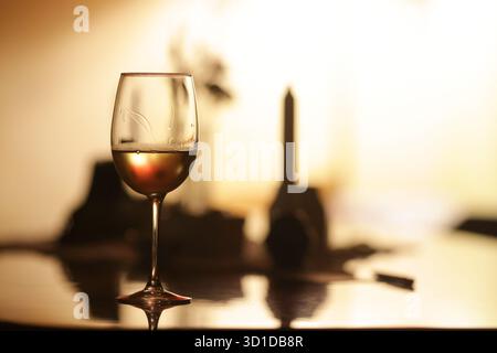Shallow depth of field (selective focus) details with a glass of white wine on a table in a dark room with back light. Stock Photo