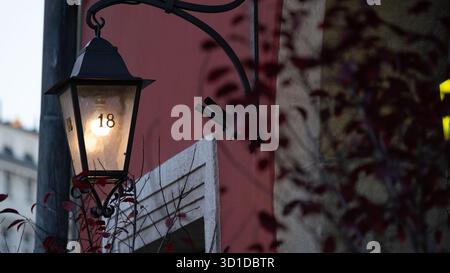 Warmly lit vintage lantern with the number 18 mounted on a red building wall at dusk. The photo captures cozy evening light and urban architectural de Stock Photo
