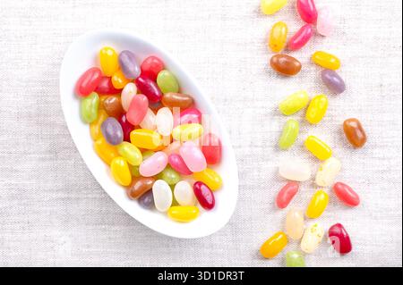 Jelly beans, flavor and color assortment, in oval white bowl, on linen. Small bean-shaped sugar candies with soft candy shells and thick gel interiors Stock Photo