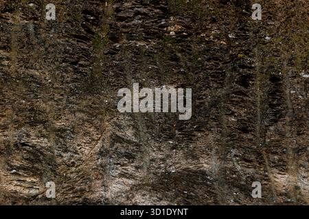 Detailed texture of a dark, layered and irregular rock wall. Rustic and organic atmosphere, mineral-rich. Ideal for background, design, geology Stock Photo