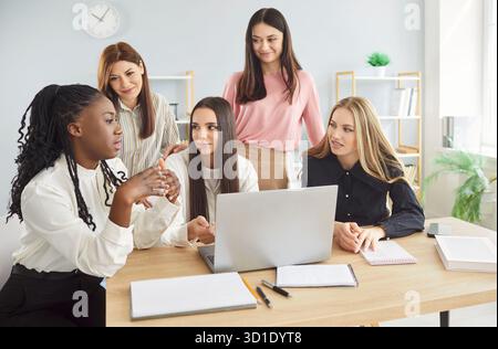 Female colleagues gathering around laptop computer, diverse women engaging in discussion Stock Photo