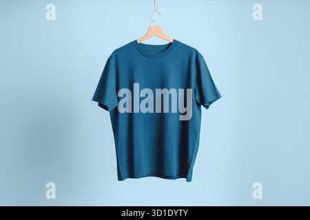 Crewneck model T-shirt in high-quality teal blue cotton, hanging on a wooden hanger. Neutral, clean, and professional background. Stock Photo