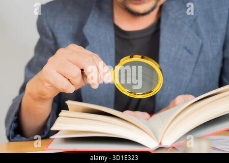 Businessman looking through a magnifying glass to a book on wooden table. Selective focus. Stock Photo