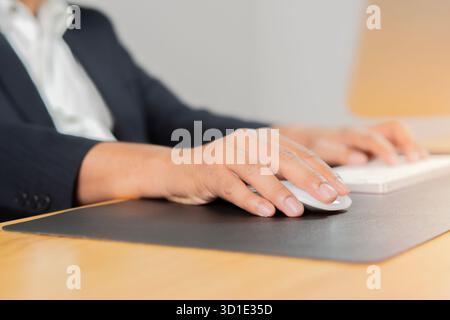 Man hand typing on computer keyboard and holding computer mouse on wooden desk at office. Selective focus. Stock Photo