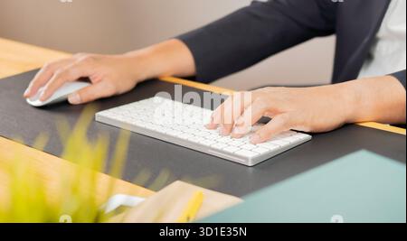 Young man in suit clicking mouse and pressing key of computer keyboard while working over new software by workplace Stock Photo