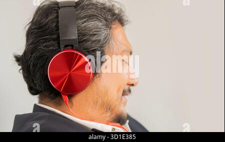 Shot of a mature businessman wearing headphones and using a cellphone over white background with copy space. Close-up Stock Photo