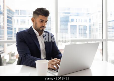 Serious young Indian executive man typing on laptop Stock Photo
