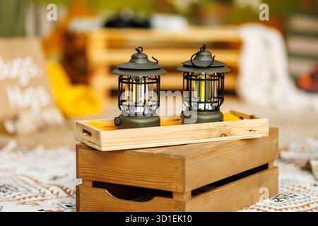 Pair of metal camping lanterns placed on wooden box in cozy home interior with warm light. Stock Photo