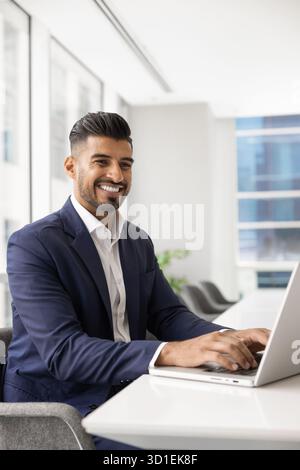 Cheerful handsome stylish young Indian businessman typing on laptop Stock Photo