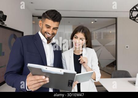 Diverse couple of positive office colleagues discussing documents on clipboard Stock Photo