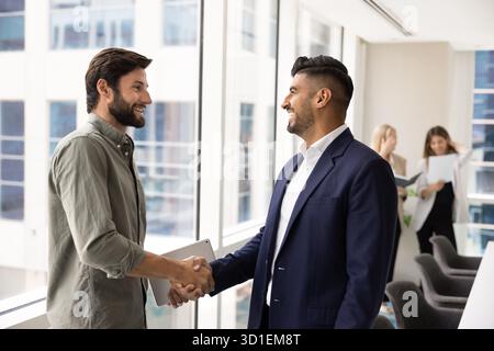 Two happy multiethnic male business coworkers shaking hands in office Stock Photo