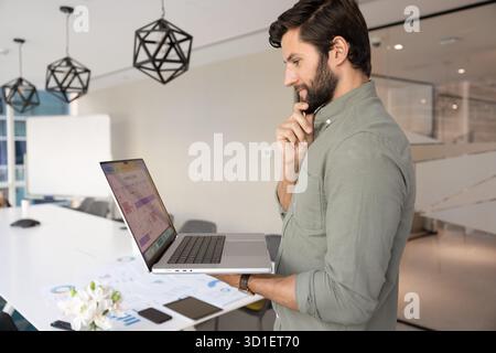 Positive thoughtful Caucasian project manager man using laptop Stock Photo