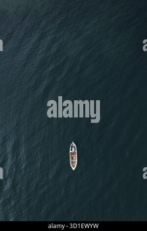 A solitary boat floating in the vast, deep blue ocean Stock Photo