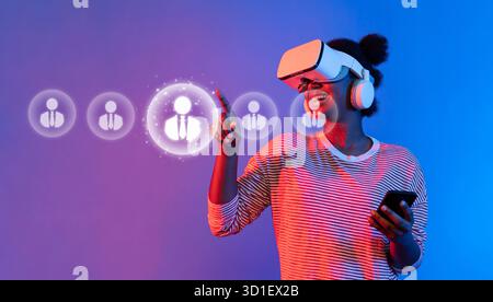 A young woman joyfully interacts with a virtual reality headset and smartphone, exploring innovative technology to connect and communicate in a vibran Stock Photo