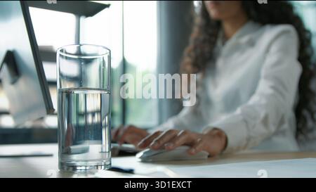 Close up glass of still water standing on table in business office blurred view unrecognizable woman businesswoman female girl worker working with Stock Photo