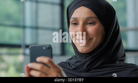 Close-up smiling Muslim business woman in hijab chatting mobile phone Arabian businesswoman female girl happy smile using smartphone at workplace Stock Photo