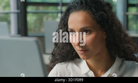 Focused Hispanic business woman working on computer in office Arabian ethnic businesswoman looking at pc monitor smiling typing browsing internet job Stock Photo