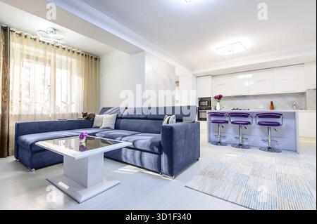 Interior of modern studio apartment with white kitchen and sofa, purple bar chairs, minimalistic clean design Stock Photo