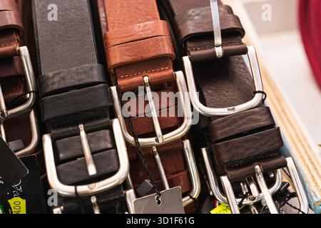 Displaying a close-up of various genuine leather belts with shiny metal buckles and price tags, highlighting craftsmanship, style, and fashion options Stock Photo