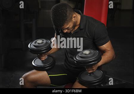 Handsome young african descent Mixed-race man sitting and resting on bench in gym Stock Photo